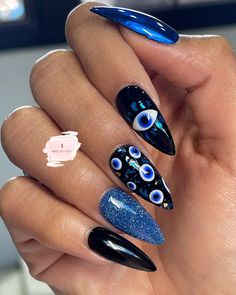 a woman's hand with blue and black nail polishes on her nails, holding an eyeball