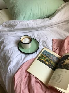 an open book, cup and saucer on top of a bed with pink sheets