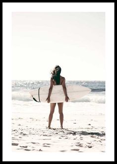 a woman standing on the beach holding a surfboard