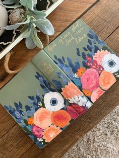 an open book sitting on top of a wooden table next to a vase with flowers