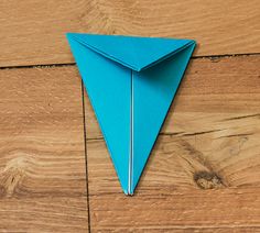 an origami blue paper airplane sitting on top of a wooden floor