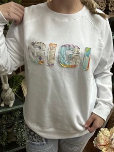 a woman wearing a white sweatshirt with the word gigi printed in multicolored letters