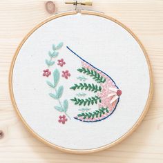 a close up of a embroidery on a wooden surface with flowers and leaves in the hoop