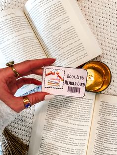 a person holding a book club member card next to an open book