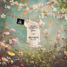 a baby's bodysuit hanging on a clothes line with flowers in the background