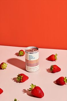 a can of soda with strawberries scattered around it on a pink table against an orange wall