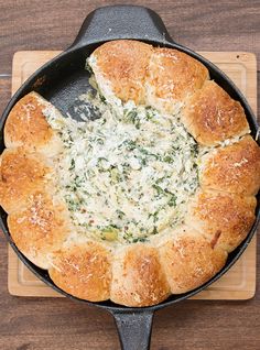 a pan filled with bread and spinach on top of a wooden cutting board