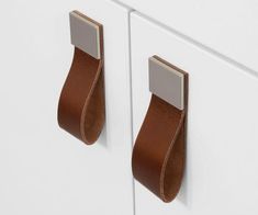 two brown leather handles on white cabinets