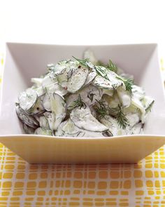 a white bowl filled with cucumber salad on top of a yellow and white table cloth