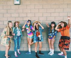 four girls are standing in front of a brick wall and one girl is holding her hand up