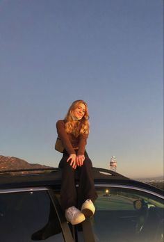 a woman sitting on the roof of a car with her legs crossed and smiling at the camera