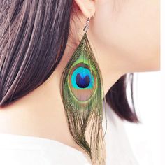 a close up of a person wearing earrings with a peacock feather