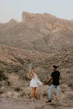 a man and woman holding hands in the desert with mountains in the backgroud