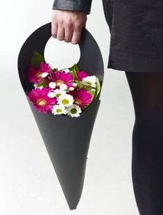 a woman is holding a black vase with flowers in it and her hand on the handle