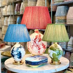 three lamps sitting on top of a table next to plates and vases in a store