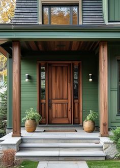 a green house with two large planters on the front porch