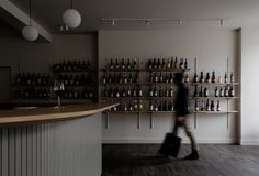 a person walking past a counter with lots of bottles on the wall and shelves behind them