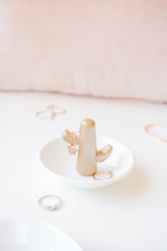 a white plate topped with a ring on top of a table next to a pink pillow