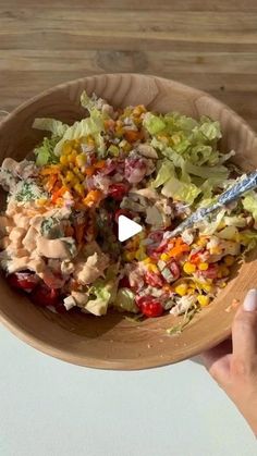 a person holding a wooden bowl filled with salad and dressing on top of a table