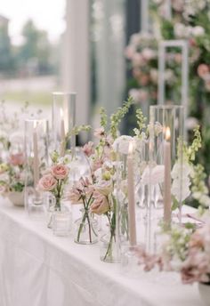 the table is set with many vases and candles, all filled with pink flowers