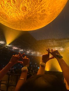 two people holding their hands up in front of a large yellow ball that is suspended from the ceiling