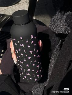 a woman is holding a black and pink flowered water bottle in her left hand