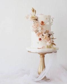 a white and gold wedding cake with flowers on the top is sitting on a stand