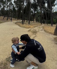 a man kneeling down next to a little boy on a skateboard in the woods