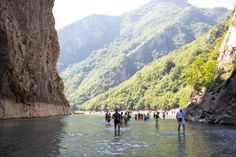 several people are wading in the water near some cliffs and mountains on a sunny day