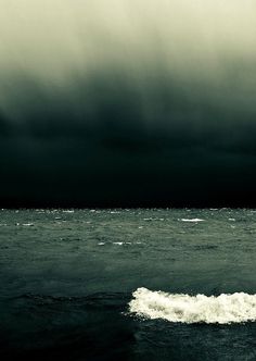 a person riding a surf board on a wave in the ocean under a cloudy sky