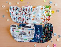 three baby bibs are laid out on a table with buttons all around them and one is in the shape of a cat