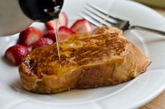 a plate with french toast and strawberries is being drizzled with syrup