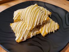 two pieces of pastry sitting on top of a black plate with white frosted icing