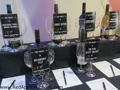 several wine bottles and glasses on a table with paper labels in front of them,