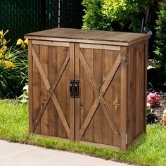 a wooden storage box sitting on the side of a sidewalk in front of some flowers