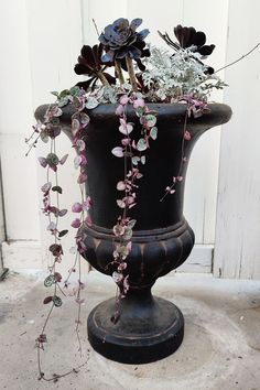 a large black vase filled with flowers on top of a cement floor next to a white door