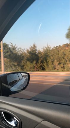 the rear view mirror of a car as it drives down a road with trees in the background