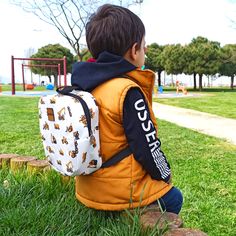 a young boy sitting in the grass with a back pack