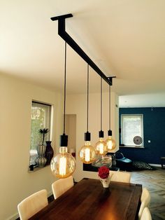 a dining room table with four lights hanging from it's center and two vases on the other side