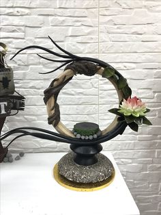 a sculpture made out of branches and flowers on a white table with a brick wall in the background