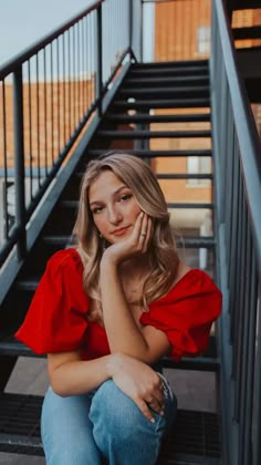 a woman is sitting on the stairs with her hand under her chin and looking at the camera