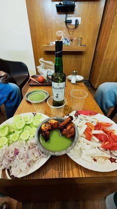 a wooden table topped with plates of food next to a bottle of wine and glasses