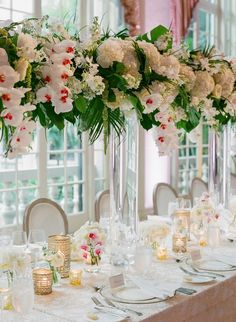 the table is set with white and pink flowers in tall glass vases on each side