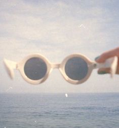 a person holding up two white sunglasses over the ocean