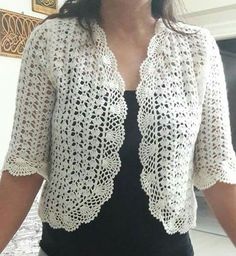 a woman standing in front of a mirror wearing a white crochet jacket