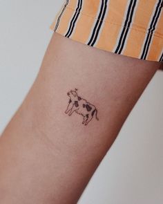 a small tattoo of a cow on the left inner arm, with black and white stripes