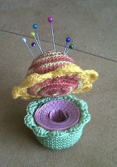 two knitted hats sitting on top of each other with pins sticking out of them