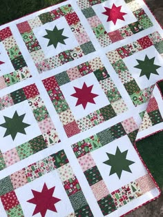 a quilted table topper with red and green stars on the center, sitting on grass