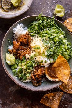 a bowl filled with meat and vegetables next to tortilla chips on a table