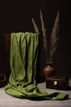 a green blanket sitting on top of a table next to a vase